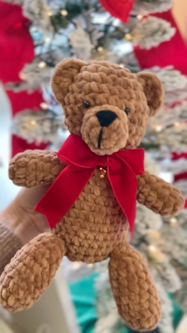 Orsetto amigurumi morbido con grande fiocco rosso, accanto all'albero di Natale